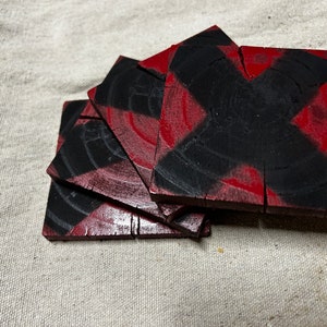 May include: Set of four red and black wooden coasters with a criss-cross pattern. The coasters are square and have a rustic look.