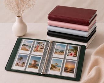 Puede incluir: Un álbum de fotos de anillas verde oscuro abierto que muestra ocho fotos instantáneas rectangulares de playas. Al lado hay una pila de cinco álbumes idénticos en burdeos, rosa, azul claro, negro y blanco, junto a un pequeño jarrón blanco.