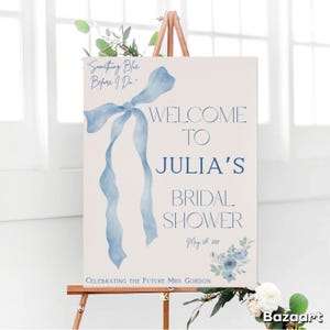 Puede incluir: Un cartel de bienvenida para una despedida de soltera con una cinta azul de acuarela y un diseño floral. El cartel dice "Welcome to Julia's Bridal Shower May 20, 2015 Celebrating the Future Mrs. Gordon"