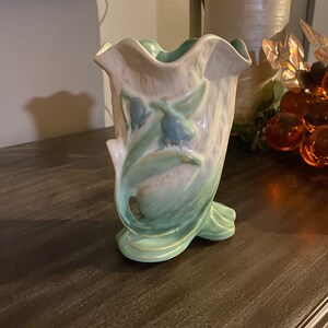 May include: A green and white ceramic vase with a ruffled top and a floral design. The vase features a stylized depiction of bluebells.