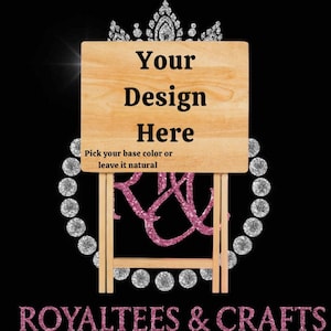 May include: A wooden sign with the text "Your Design Here" and "Pick your base color or leave it natural". The sign is supported by a wooden frame, with a pink glitter design and the words "ROYALTEES & CRAFTS" at the bottom.