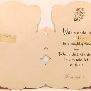 Op de afbeelding: Vintage wenskaart in de vorm van een beer. De kaart is cr&egrave;mekleurig met een kleine illustratie van een beer met een hart. De tekst op de kaart luidt: "Met heel veel liefde...Aan een geweldige zoon..." en "Raad eens wie?"