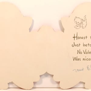Op de afbeelding: Vintage Valentijnsdagkaart in een wolkvorm, cr&egrave;mekleurig. De rechterkant heeft een tekening van een katje en handgeschreven tekst: "Honest to goodness, Just betcha it's true No Valentine ever Was nicer than you!" Ondertekend "mis Elmblade".