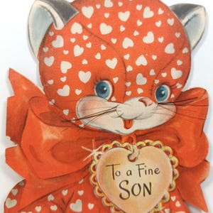 Op de afbeelding: Vintage Valentijnsdagkaart met een cartoonkat met oranje vacht en witte hartpatronen. De kat heeft blauwe ogen, een rode strik en een hartvormig label met de tekst "To a Fine SON".