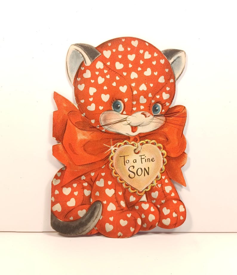 Op de afbeelding: Vintage Valentijnsdagkaart met een cartoonkat met een rode body bedekt met witte hartjes. De kat heeft blauwe ogen, een rode strik en een hartvormig label met de tekst "To a Fine SON". Een nostalgisch en charmant ontwerp.