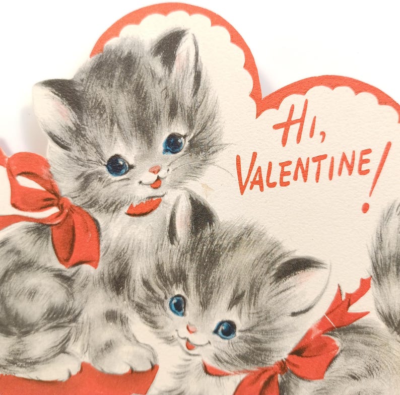 Op de afbeelding: Vintage Valentijnsdagkaart met twee grijze kittens met blauwe ogen en rode strikken. De kaart heeft een hartvormig ontwerp met de woorden "Hi, Valentine!" in rode letters. Een charmante en nostalgische wenskaart.