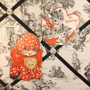 Op de afbeelding: Vintage Valentijnskaarten met kattenillustraties. E&eacute;n kaart toont een rode kat met hartpatronen en de tekst "To a Fine Son". Een andere kaart toont twee grijze kittens met rode strikken en de tekst "Hi, Valentine!"