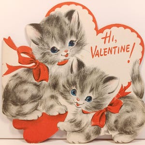 Op de afbeelding: Vintage Valentijnsdagkaart met twee grijze kittens met blauwe ogen en rode strikken. De kittens omarmen een rood hart. De kaart heeft de tekst "Hi, Valentine!" in het rood.