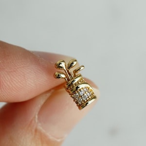 Op de afbeelding: Een gouden golfbag-bedel met heldere zirkonia-stenen. De bedel is klein en delicaat, perfect om een ​​persoonlijke touch toe te voegen aan een ketting of armband.