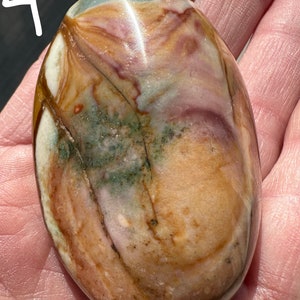 May include: A smooth, oval-shaped stone with a unique pattern of brown, pink, white, and green colors. The stone has a polished finish and is a natural specimen.