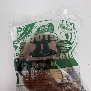 Peut inclure: Un jouet en peluche marron dans un sachet en plastique transparent Sonic Wacky Pack. L'emballage présente des graphismes verts, le texte Zoo Tots, Monkey Tot et une adresse web. Le sachet inclut des avertissements et une encoche d'ouverture.