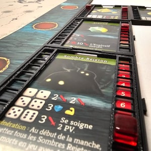 Puede incluir: Un juego de cartas en blanco y negro con una carta de personaje oscuro que muestra una criatura con ojos brillantes. La carta tiene el texto "Sombre Rejeton" y "Se soigne 2 PV". La carta est&aacute; rodeada de un marco negro con dados rojos y blancos.