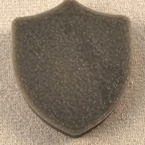 May include: A dark gray shield-shaped soap bar with a textured surface.
