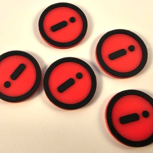 May include: Five red and black circular tokens with a black exclamation point and a black dot on each. The tokens are made of plastic and have a textured surface.