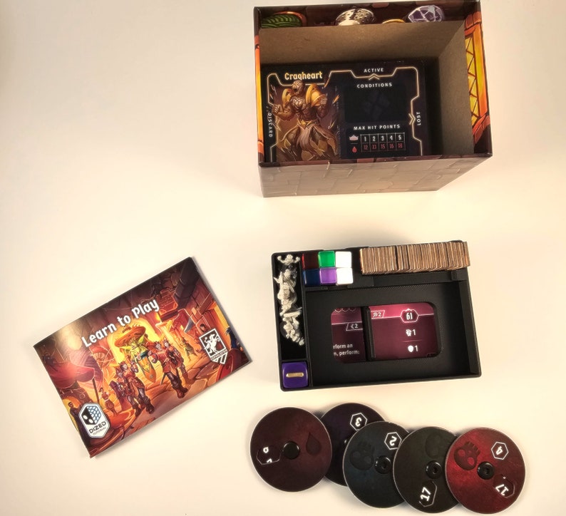 May include: A board game with a learn to play guide, a box with a character card, a game board with tokens, and five black and red discs with numbers on them.