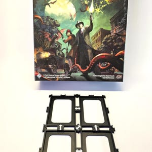 Könnte beinhalten: Die Schachtel des Brettspiels Arkham Horror: The Card Game zeigt auf der Vorderseite einen dunkelgrünen Hintergrund mit einem Vollmond, zwei Ermittlern und einem monströsen Tentakel. Der Text "Arkham Horror: The Card Game" ist in Weiß auf einem schwarzen Banner gedruckt.