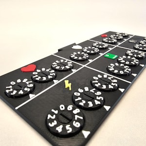May include: A black game board with a grid of numbered dials. The dials are white with black numbers and have a red heart and a green square in the centre. The board also has a lightning bolt symbol.
