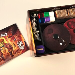 May include: A board game box with a brown and orange exterior. The box is open and shows the game's components, including dice, cards, and miniature figures. The box also includes a booklet titled "Learn to Play".