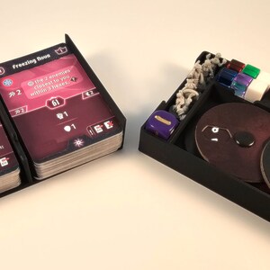 May include: A black plastic organizer with two card holders, two circular trays, a dice tray, and a stack of cards. The card holders have the text "Twin Beams" and "Freezing Boost" on them. The circular trays have the numbers 17, 18, and 19 on them. The dice tray has a purple die in it.