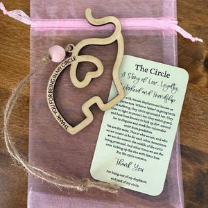 May include: A wooden elephant-shaped charm with the text "THANK YOU FOR BEING IN MY CIRCLE" and a pink bead, presented in a pink mesh bag. A card with text about love, loyalty, sisterhood, and friendship is also included.