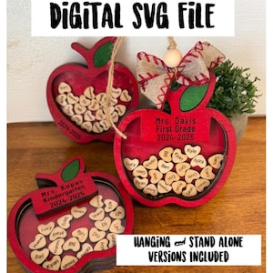 May include: Three red apple-shaped wooden ornaments with a clear window to display names. Each ornament has a hanging loop and a personalized label with the teacher's name and grade level. The text on the labels reads "Mrs. Kopas Kindergarten 2024-2025", "Mrs. Davis First Grade 2024-2025", and "Hanging and Stand Alone Versions Included".