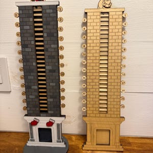 May include: Two wooden Christmas advent calendars shaped like chimneys. One is gray with red stockings, the other is natural wood. Each has a Santa figure on top and numbers 1-24.