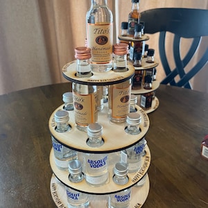 May include: A three-tiered wooden stand with a circular base, designed to hold miniature liquor bottles. The stand is decorated with the text "Happy Birthday Ben". The stand is filled with miniature bottles of Tito's Handmade Vodka and Absolut Vodka.