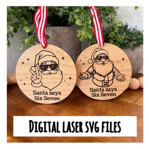 Puede incluir: Dos adornos navideños de madera con diseños de Papá Noel. Un Papá Noel hace el signo de la paz, el otro tiene los brazos abiertos. Ambos llevan gafas de sol y el texto dice "Santa says Six Seven". Cada adorno tiene una cinta a rayas rojas y blancas.