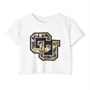May include: White crop top with a black and gold "CU" graphic. The graphic has a camouflage pattern inside the letters and a black border. The top has short sleeves and a crew neck.