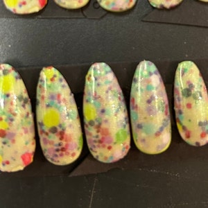 May include: Set of six white oval-shaped false nails with a colorful confetti design.