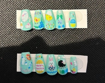 Puede incluir: Conjunto de diez uñas artificiales de color verde pastel con diseños de temática de Pascua. Los diseños incluyen conejos, pollitos, huevos y las palabras "Feliz Pascua".