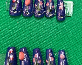 Puede incluir: Diez uñas postizas azules en forma de ataúd con acabado de purpurina plateada. Cada uña está decorada con una flor rosa y hojas verdes.