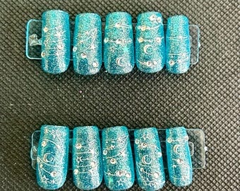 May include: Ten blue press-on nails with silver glitter and moon and star designs.