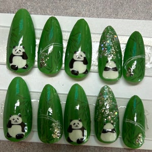 May include: Ten green and white panda bear nail tips with a bamboo design. The nail tips are long and oval shaped.