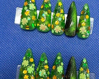 May include: Set of ten green and gold glitter press-on nails with shamrock and star designs.  The nails are in a stiletto shape.