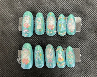 Puede incluir: Conjunto de diez uñas postizas ovaladas de color azul verdoso con purpurina y diseños de conejos blancos.