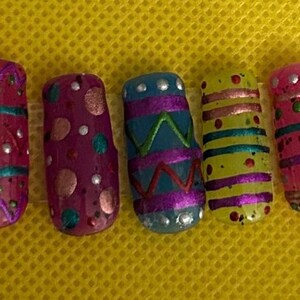 Puede incluir: Cinco diseños de arte de uñas coloridos con patrones geométricos y acentos de brillo. Los diseños incluyen colores rosa, morado, azul, amarillo y verde.