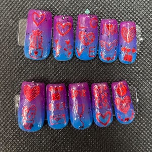 Puede incluir: Conjunto de diez uñas postizas con un diseño degradado en tonos de morado y azul. Las uñas presentan purpurina roja y detalles de lámina roja con varios diseños temáticos de San Valentín, incluyendo corazones, flores y la palabra "LOVE".