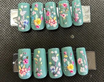 Puede incluir: Conjunto de diez uñas postizas verde azulado con diseños florales. Cada uña tiene un patrón floral diferente en tonos de rosa, amarillo, azul y verde.