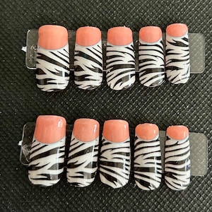 May include: Set of ten artificial nails with a zebra print design in black and white. The tips of the nails are painted a solid peach color. The nails are arranged in two rows of five on a clear plastic backing.
