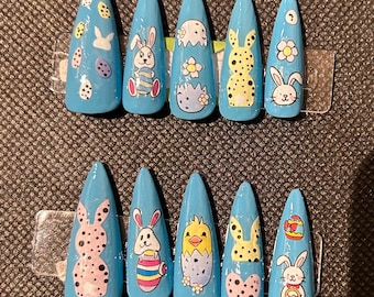 Puede incluir: Conjunto de diez uñas postizas azules con diseños de temática de Pascua. Los diseños incluyen conejos, huevos, pollitos y flores.