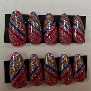 May include: Ten pink and white almond-shaped press-on nails with a diagonal glitter stripe design in pink, blue, and gold.