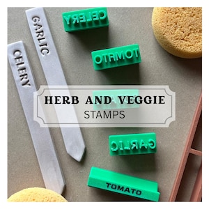 May include: A collection of herb and veggie stamps and plant markers. The stamps are bright green and read "CELERY", "GARLIC", and "TOMATO". The plant markers are white and read "CELERY" and "GARLIC". The text "HERB AND VEGGIE STAMPS" is in a white banner.