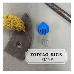 May include: A collection of pottery tools and a blue Virgo zodiac sign stamp. The stamp is round with the Virgo symbol. A brown pottery rib, yellow sponge, and a metal tool are also present. The text "ZODIAC SIGN STAMP" is displayed on a white label.