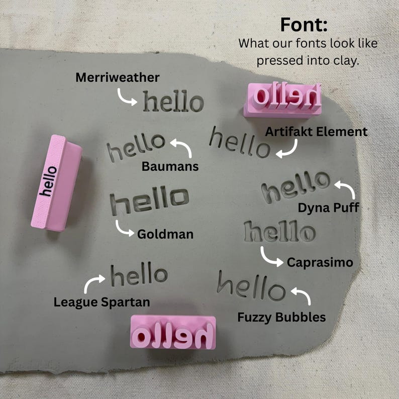 May include: A grey slab of clay featuring multiple impressions of the word hello in various typefaces, including Merriweather, Baumans, Goldman, League Spartan, Artifakt Element, Dyna Puff, Caprasimo, and Fuzzy Bubbles, with two pink stamps.