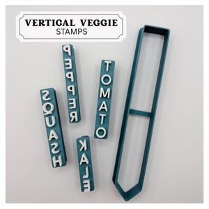 May include: A set of teal and white vertical veggie stamps featuring the text VERTICAL VEGGIE STAMPS. The set includes four rectangular stamps with the words SQUASH, PEPPER, TOMATO, and KALE in white raised letters on teal bases, plus a long frame.