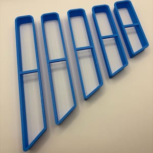 May include: Five blue plastic cookie cutters in a rectangular shape with a horizontal bar. The cutters are arranged diagonally, with a white background. The cutters are likely for baking or crafting.