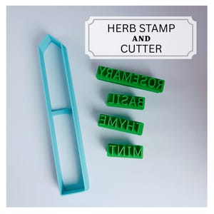 May include: A light blue elongated hexagonal cookie cutter and four green rectangular stamps with the text HERB STAMP AND CUTTER. The stamps feature the embossed words ROSEMARY, BASIL, THYME, and MINT in a clear, sans-serif font for culinary use.