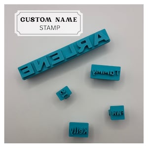 May include: A set of five teal custom name stamps featuring raised lettering. The stamps display the names ARLENE, TAMMY, SI, HWH, and KELLY in various rectangular and square block formats. A white label at the top displays the text CUSTOM NAME STAMP.
