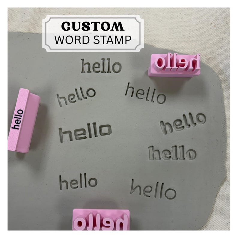 May include: A light pink custom word stamp with the text hello, shown alongside a grey clay slab featuring multiple impressions of the word hello. A white rectangular label at the top displays the black text CUSTOM WORD STAMP in a serif font.